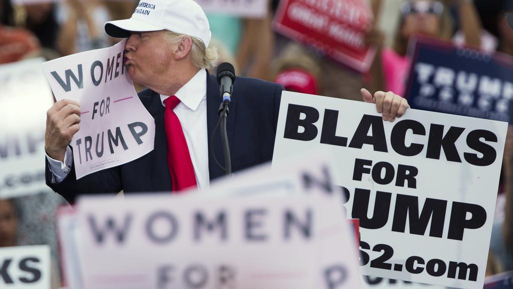 Donald Trump embrassant un panneau indiquant "Les femmes pour Trump" lors d'un meeting le 12 octobre 2016. [Keystone - Evan Vucci]