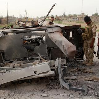 Des membres des forces armées irakiennes inspectent les restes d'un véhicule du groupe Etat islamique (image d'illustration). [AFP - Moadh al-Dulaimi]