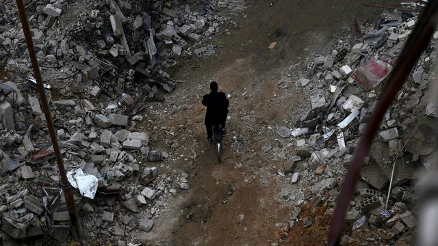 Un homme traverse les ruines d'un quartier de Damas à vélo. [Bassam Khabieh]