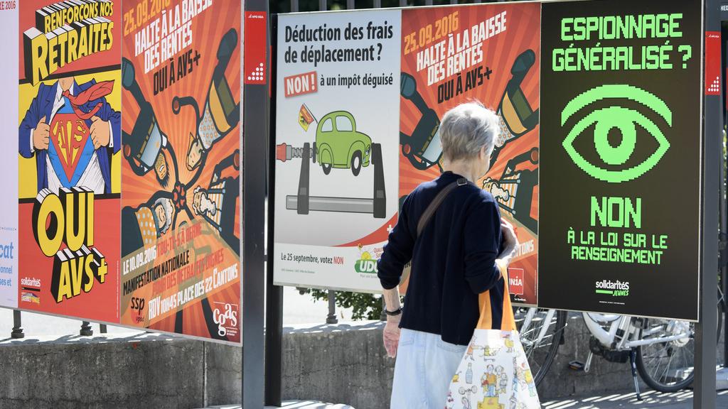 Une personne passe devant des affiches sur les différents thèmes des votations fédérales et cantonales à Genève. [Keystone - Martial Trezzini]