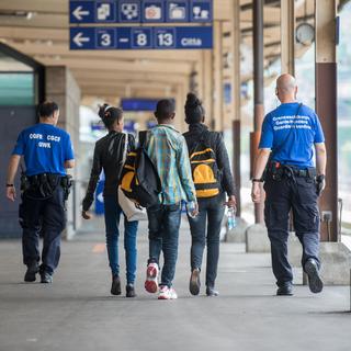 Un groupe de migrants escorté par des gardes-frontière à la gare de Chiasso. [KEYSTONE - Ti-Press/Francesca Agosta]