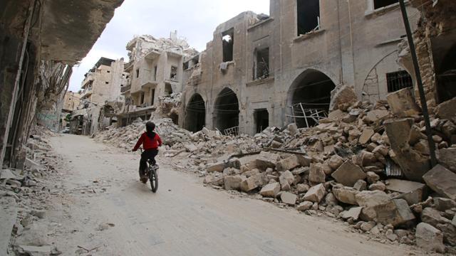 Un garçon sur un vélo passe près d'immeubles endommagés à Alep. [Abdalrhman Ismail]