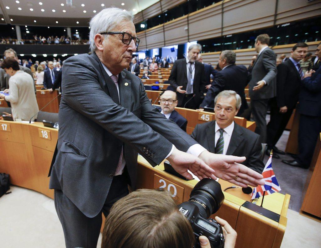 Jean-Claude Juncker au Parlement européen mardi, tentant d'empêcher des photographes de s'intéresser à Nigel Farage. [Keystone - OLIVIER HOSLET]