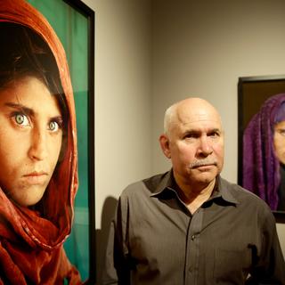 Le photographe Steve McCurry pose devant ses deux photos de l'Afghane, l'une prise en 1984 et la seconde en 2002. [AFP - ULRICH PERREY]