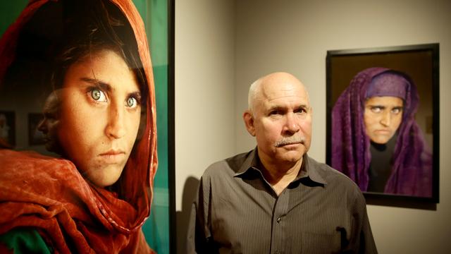 Le photographe Steve McCurry pose devant ses deux photos de l'Afghane, l'une prise en 1984 et la seconde en 2002. [AFP - ULRICH PERREY]