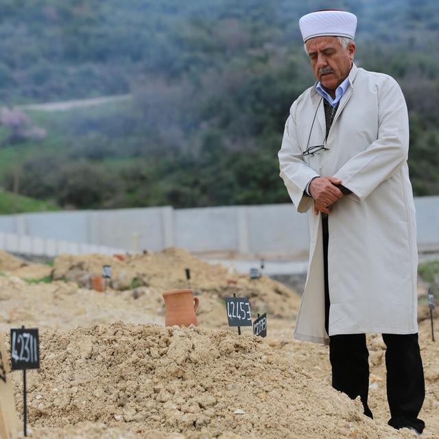 Un homme prie sur une tombe du cimetière turc d'Izmir, où de nombreux migrants non identifiés sont enterrés. [AP Photo / Keystone - Dominique Soguel]