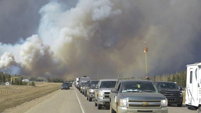 De longues files de voitures remontaient vers le nord sur l'autoroute au coeur de la ville au milieu des flammes. [Greg Halinda/The Canadian Press]