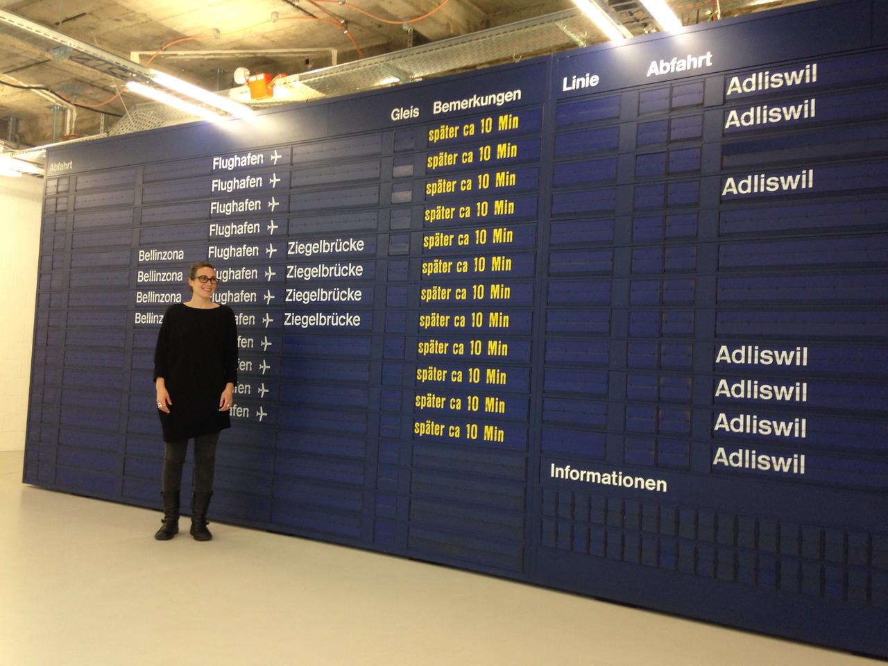 Caroline Hirt, co-fondatrice du MuDA, devant l’ancien panneau CFF de la gare de Zurich, pièce maîtresse du musée. [RTS - Rouven Gueissaz]