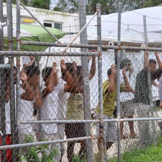Des demandeurs d'asile regardent à travers la grille du centre de Manus. [Reuters - Eoin Blackwell]