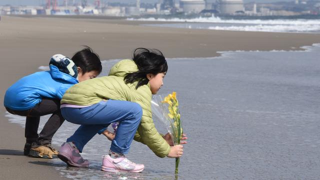 Une soeur et son frère ont mis des fleurs sur la plage de Sendai, le 11 Mars 2016, pour rendre hommage aux victimes du séisme et du tsunami qui ont frappé le Japon en 2011. [AFP - Toru Yamanaka]