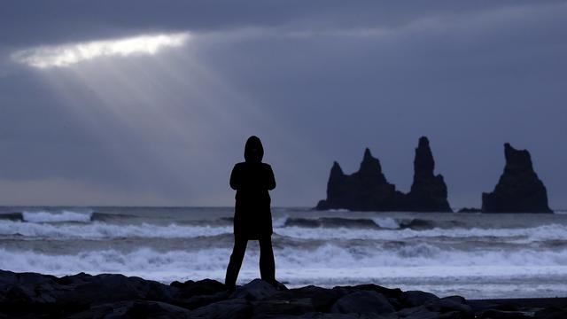 Une touriste sur le sable noir de Vik, près du volcan Katla, en Islande, en octobre 2016. [Keystone - Frank Augstein]