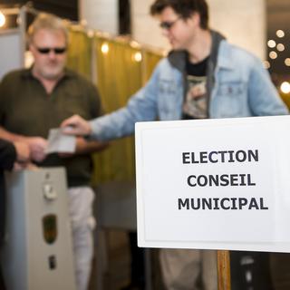 Une personne glisse son enveloppe de vote dans l'urne a l'intérieur du bureau de vote lors du premier tour des élections municipales en Valais. [Keystone - Jean-Christophe Bott]