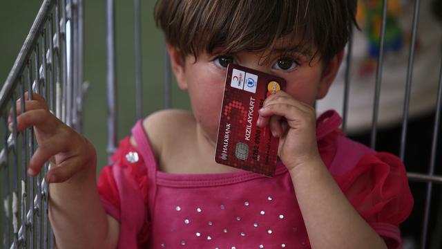 Une fillette réfugiée syrienne à Gaziantep, en Turquie, tient une carte de crédit fournie par le Programme alimentaire mondial (PAM) pour les couvrir partiellement les achats de la famille. [Lefteris Pitarakis]