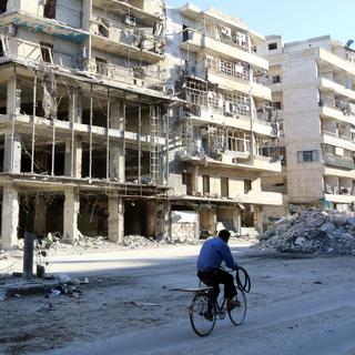 Un homme passe en vélo près d'immeubles endommagés à Alep. [Reuters - Abdalrhman Ismail]