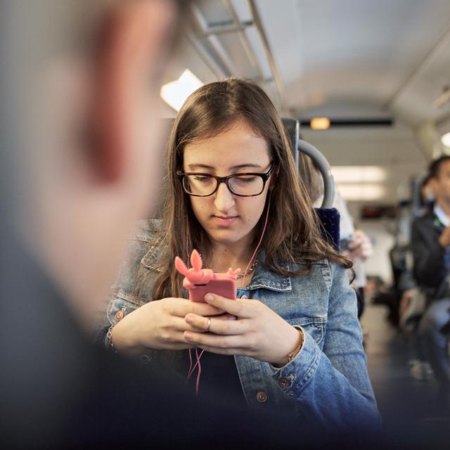 Une jeune femme utilise son téléphone portable lors d'un trajet dans un train. [Keystone - Christof Schuerpf]