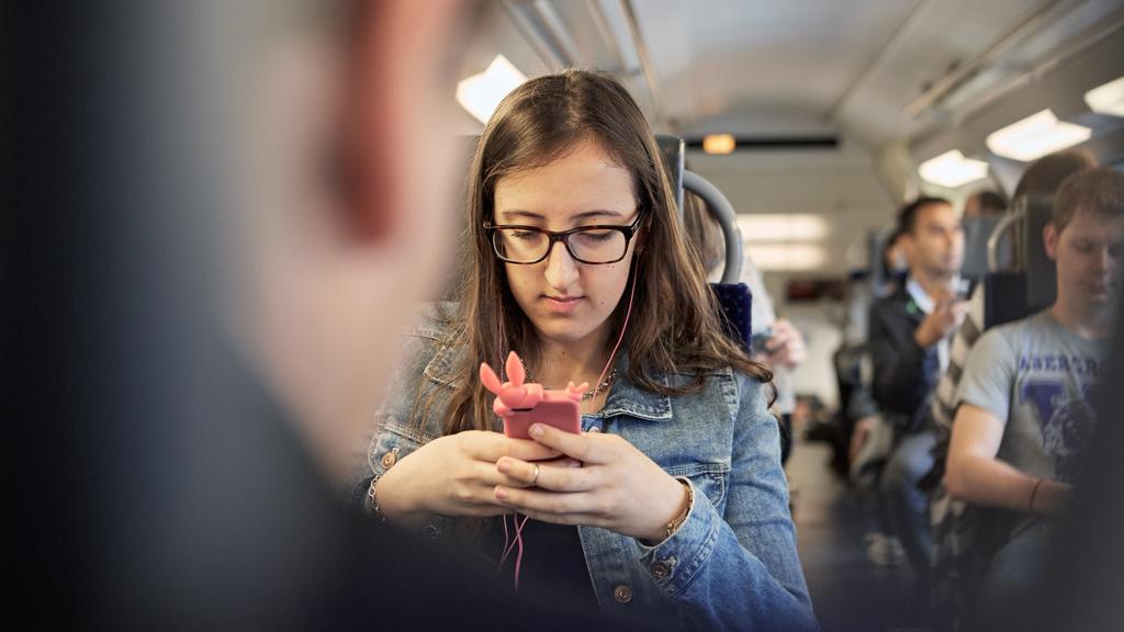 Une jeune femme utilise son téléphone portable lors d'un trajet dans un train. [Keystone - Christof Schuerpf]