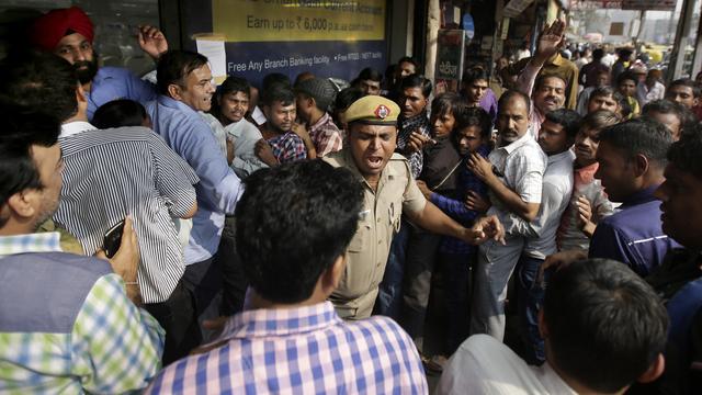 Un policier indien tente de contenir la foule qui fait la queue à l'extérieur d'une banque à New Delhi. [Keystone - AP Photo/Altaf Qadri]