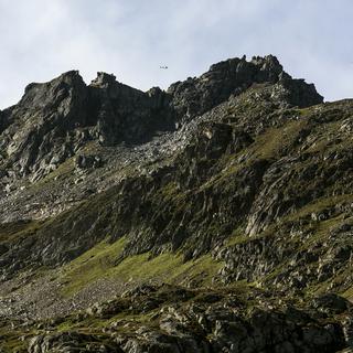Un hélicoptère participant aux recherches du F-A-18 de l'armée suisse porté disparu le 29 août apparaît au-dessus des montagnes dans la région du Susten. [Keystone - Alexandra Wey]