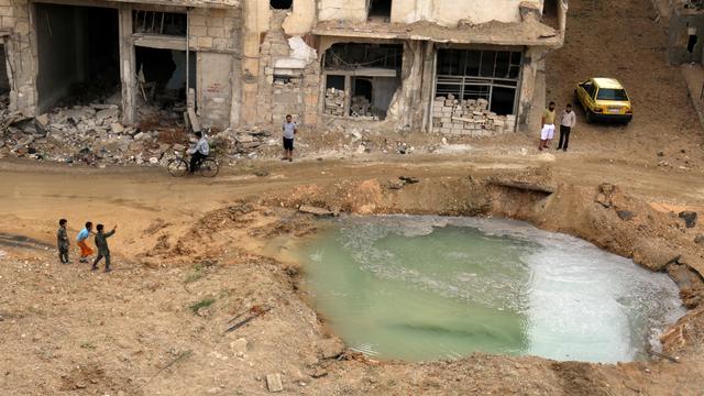 Des habitants inspectent un cratère rempli d'eau dans le quartier rebelle de Tariq al-Bab à Alep. [Reuters - Abdalrhman Ismail]