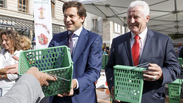 Guillaume Barazzone (à gauche) et Luc Barthassat (à droite) distribuent des poubelles vertes à Genève. [Keystone - Salvatore Di Nolfi]