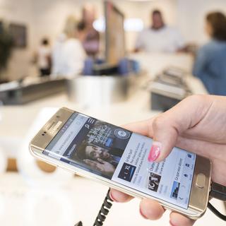 Un client teste un téléphone mobile dans un Swisscom shop à Lausanne. [Keystone - Christian Beutler)]