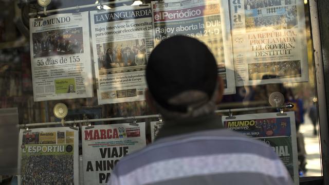 Un homme lit les gros titres de la presse espagnole dans un kiosque de Barcelone. [Keystone - AP Photo/Francisco Seco]