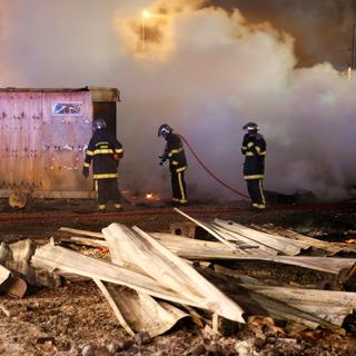 Des pompiers en train d'éteindre les feux qui détruisent les cabanons en bois du camp de migrants de Grande-Synthe, près de Dunkerque (F). [Reuters - Pascal Rossignol]