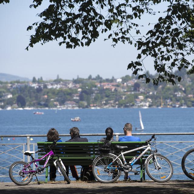 Quatre personnes assises sur un banc à la Perle du Lac, à Genève. [Keystone - Martial Trezzini]