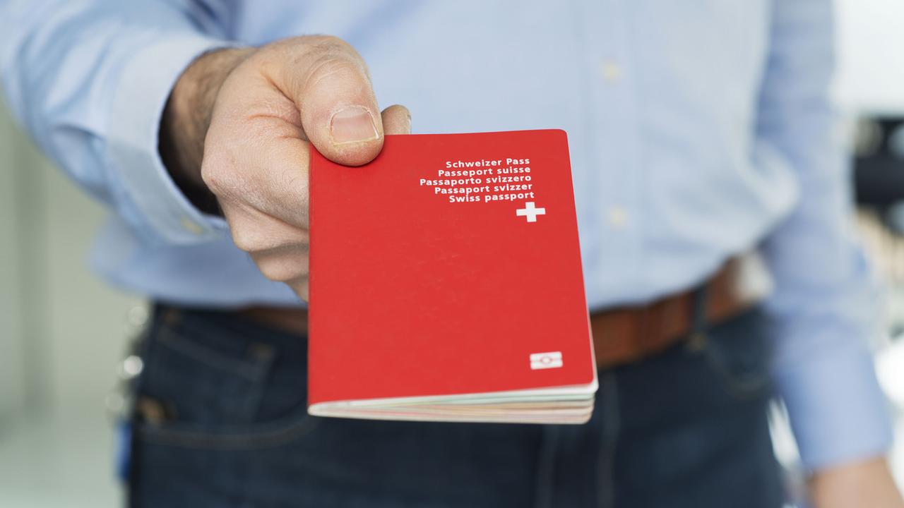 Un homme tenant un passeport suisse dans sa main. [Keystone - Christian Beutler]