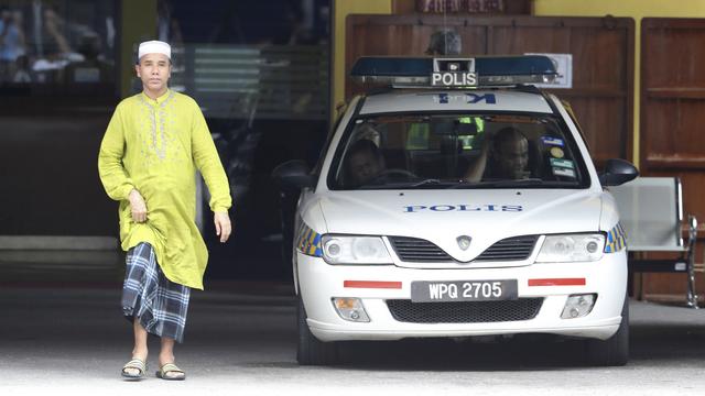 Un homme passe près d'une voiture de police garée devant l'institut de médecine légale de Kuala Lumpur, qui enquête sur la mort de Kim Jong-Un, demi-frère du leader nord-coréen. [Keystone - AP Photo/Vincent Thian]