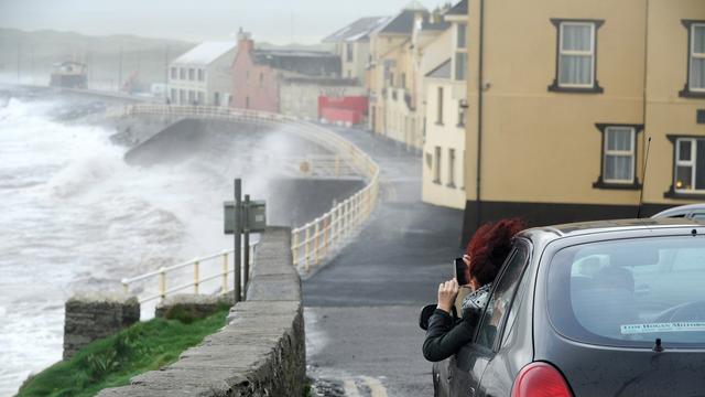 Une femme filme les vagues qui déferlent sur le village de Lahinch, sur la côte irlandaise. [Keystone - EPA/AIDAN CRAWLEY]