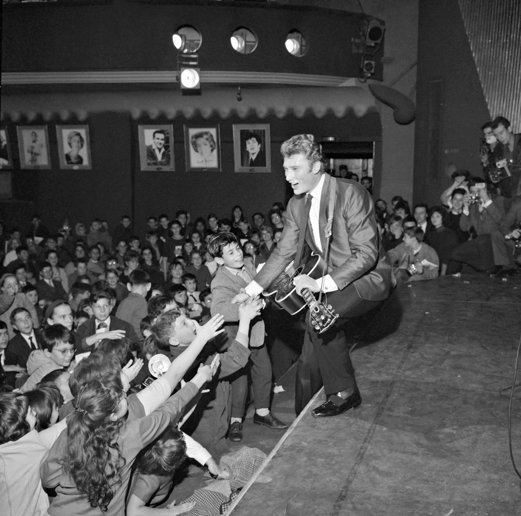 Le chanteur Johnny Hallyday chante devant 3000 enfants enthousiastes qui assistaient ensuite à la première projection du film "Mandrin", dans la salle parisienne de l'Olympia le 13 décembre 1962. [AFP]