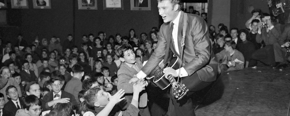 Le chanteur Johnny Hallyday chante devant 3000 enfants enthousiastes qui assistaient ensuite à la première projection du film "Mandrin", dans la salle parisienne de l'Olympia le 13 décembre 1962. [AFP]