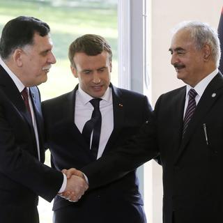 Le Premier ministre du gouvernement libyen d'union nationale Fayez al-Sarraj (à gauche) et le général Khalifa Haftar (à droite) se serrent la main, sous les yeux du président français Emmanuel Macron. [AFP - Jacques Demarthou]
