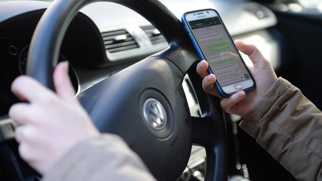 Un automobiliste tenant son volant et son smartphone (image prétexte). [Keystone - Monika Skolimowska/DPA]