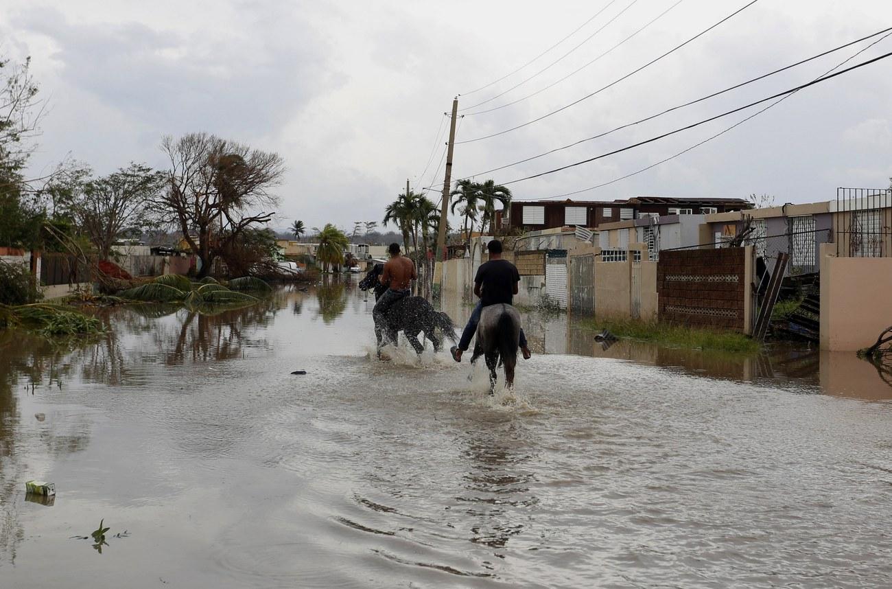 Des hommes chevauchent dans les rues inondées de Toa Baja, à Porto Rico. [Keystone - Thais Llorca]