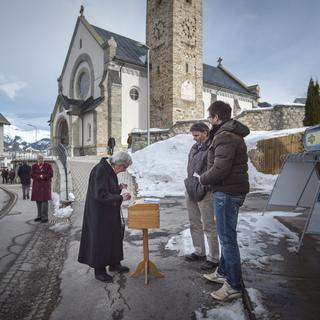 Une habitante du village grison d'Obersaxen Meierhof dépose son bulletin de vote dans l'urne, à côté de l'église du village. [Keystone - Benjamin Manser]