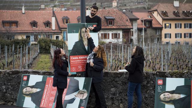 Des militants accrochent des affiches électorales représentant les trois candidats du PS vaudois en course pour les sièges du gouvernement. [Jean-Christophe Bott]