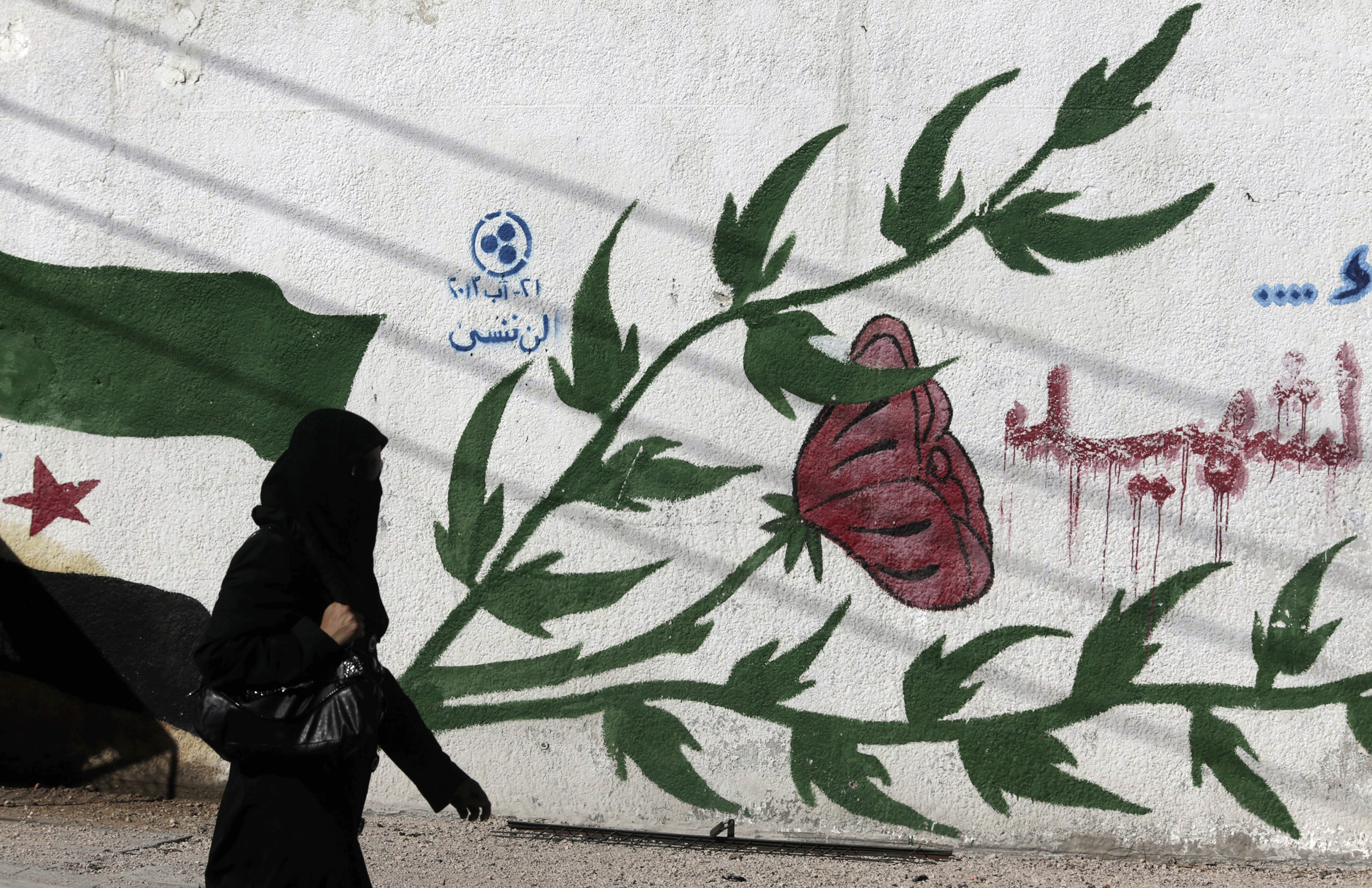 Une femme passe devant un graffiti à l'est de Ghouta en Syrie [Reuters - Bassam Khabieh]