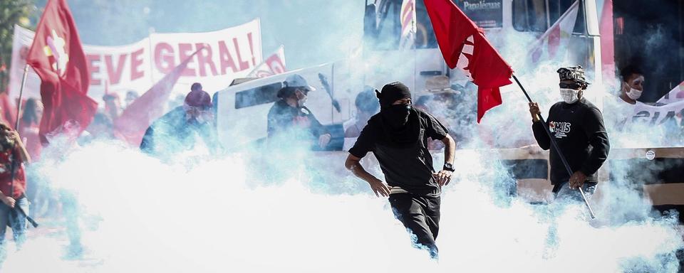 Des manifestants au milieu des fumigènes des forces de police lors d'un rassemblement contre le président Temer à Brasilia. [Keystone - Fernando Bizerra Jr.]