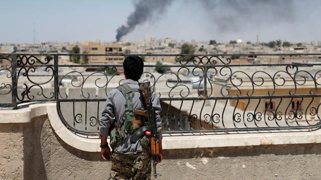 Un combattant kurde des Unités de protection du peuple (YPG) regarde au loin de la fumée après une frappe de la coalition internationale à Raqa, en Syrie. [Goran Tomasevic]