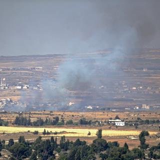 De la fumée s'élève après des tirs sur un village syrien proche de la frontière israélienne, sur le plateau du Golan. [Keystone - Atef Safadi]