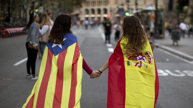 Deux adolescentes, l'une avec le drapeau catalan, l'autre avec le drapeau espagnol, photographiées main dans la main à Barcelone le 3 octobre. [AP Photo/Keystone - Emilio Morenatti]