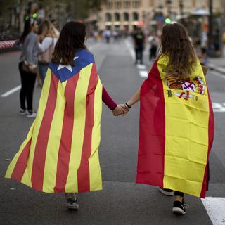 Deux adolescentes, l'une avec le drapeau catalan, l'autre avec le drapeau espagnol, photographiées main dans la main à Barcelone le 3 octobre. [AP Photo/Keystone - Emilio Morenatti]