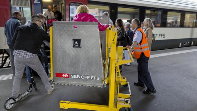 Un employé des CFF aide une personne en chaise roulante à grimper dans le train. [Gaetan Bally]