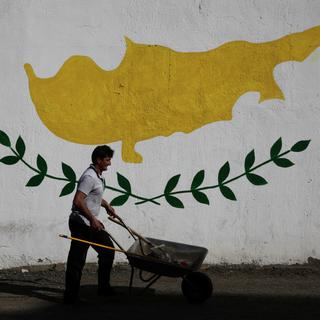 Un homme et sa brouette devant une fresque murale représentant l'île de Chypre. [Reuters - Yiannis Kourtoglou]