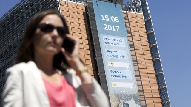 Une femme et son téléphone portable à Bruxelles devant une affiche annonçant la fin des frais d'itinérance en Europe. [EPA/Keystone - Olivier Hoslet]