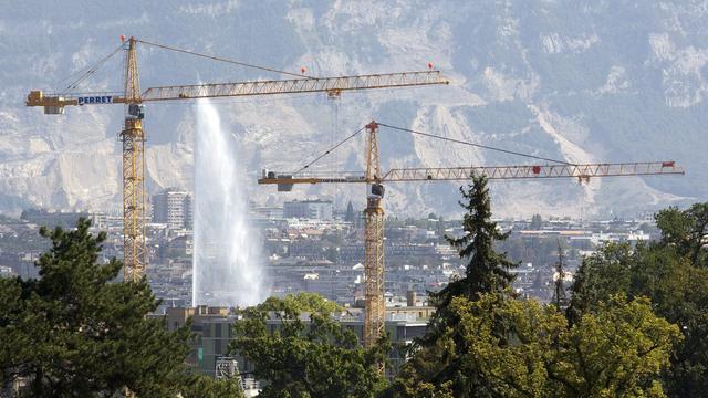 Deux grues travaillent sur un chantier pour la construction d'un immeuble avec comme fond le jet d'eau, ce lundi 22 aout 2011 a Geneve. (KEYSTONE/Salvatore Di Nolfi) [KEYSTONE - Salvatore Di Nolfi]