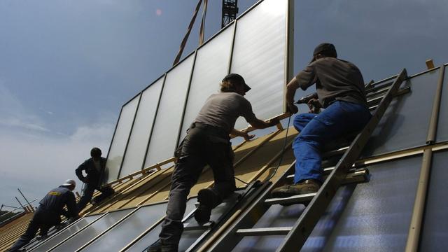 Des ouvriers en train d'installer des panneaux solaires classiques de couleur bleu-noir sur le toit d'une maison en 2006. [Keystone - Lukas Lehmann]