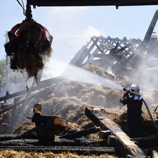 Des pompiers à l'oeuvre sur le site d'un incendie qui a complètement détruit une ferme, le 29 juillet 2017 à Payerne. [Keystone - Christian Brun]